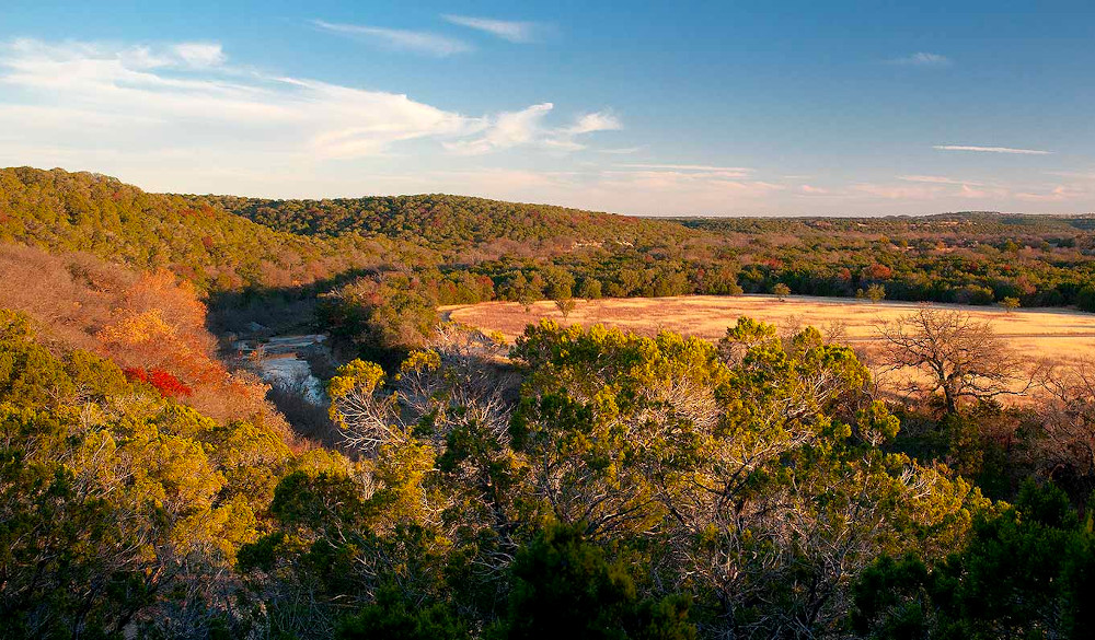 A river cuts through hills of trees in fall colors and a plateau. 