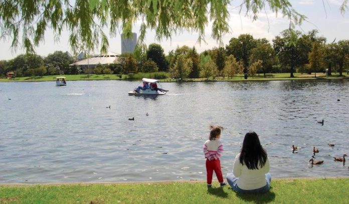 A woman and child sit near a lake at Hermann Park
