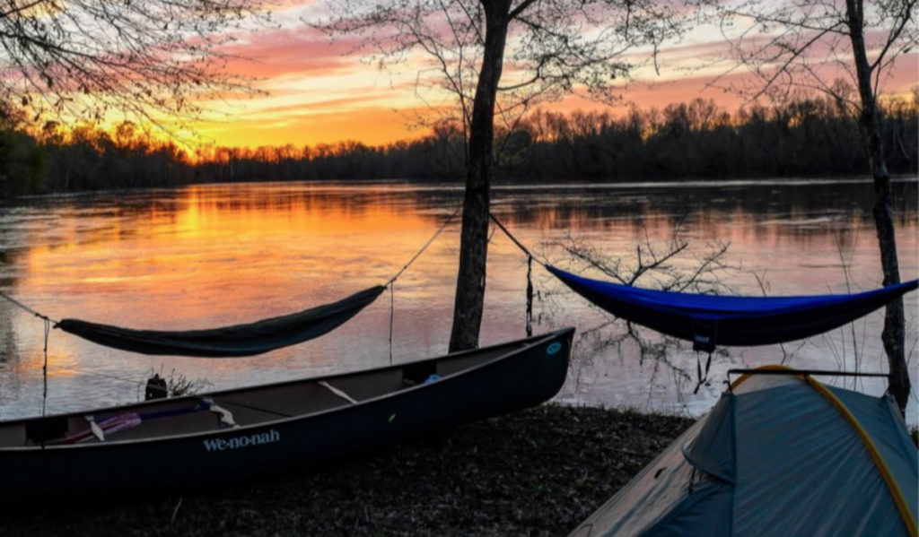 A camping site at sunset with hammocks, kanoe and tent