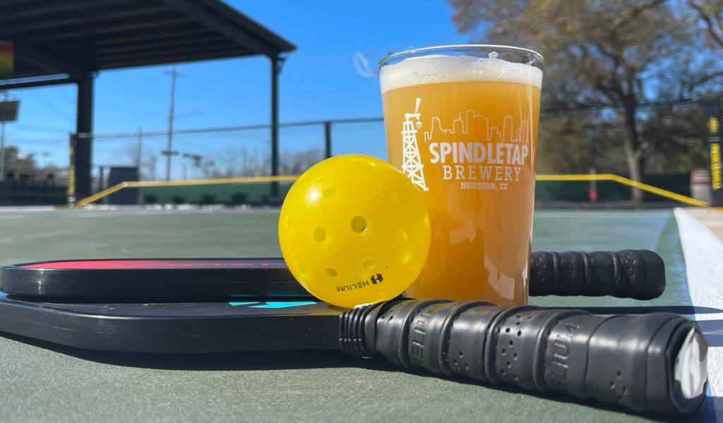A pint of beer with a pickleball and two racquets