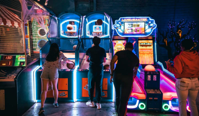 People play a basketball arcade game in a dimly lit arcade