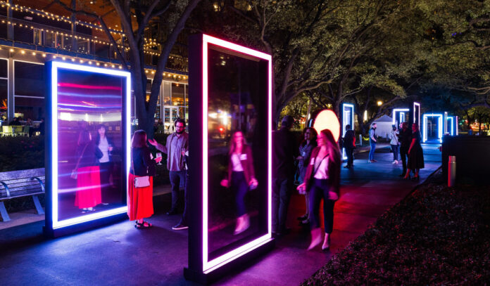 A neon art installation with mirrors and people in a park