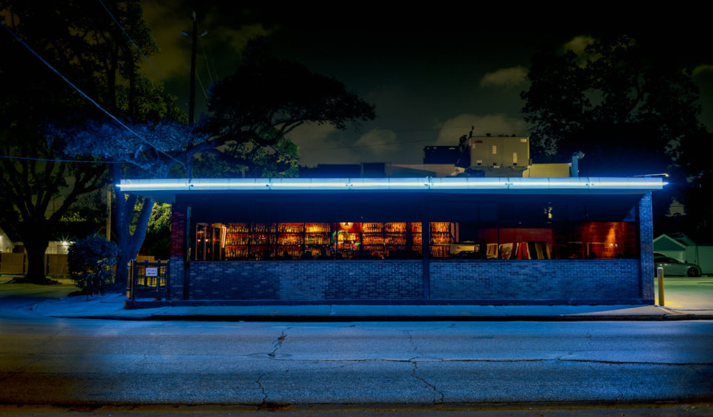 An exterior shot of a bar that is warmly lit inside