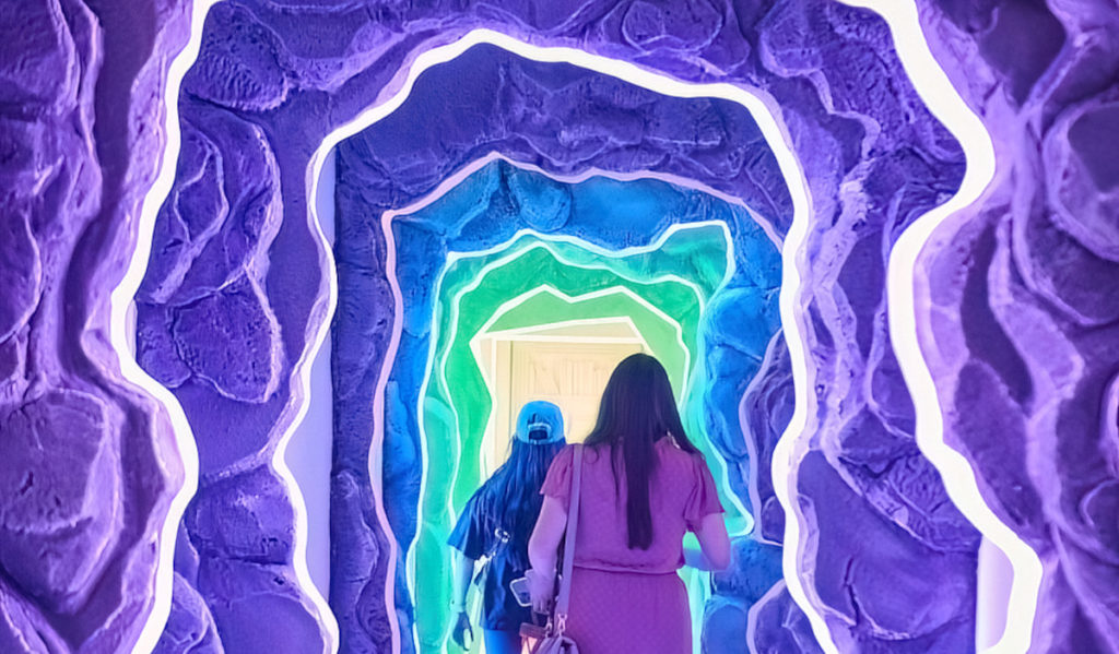 Two guests walk through a purple-lit tunnel