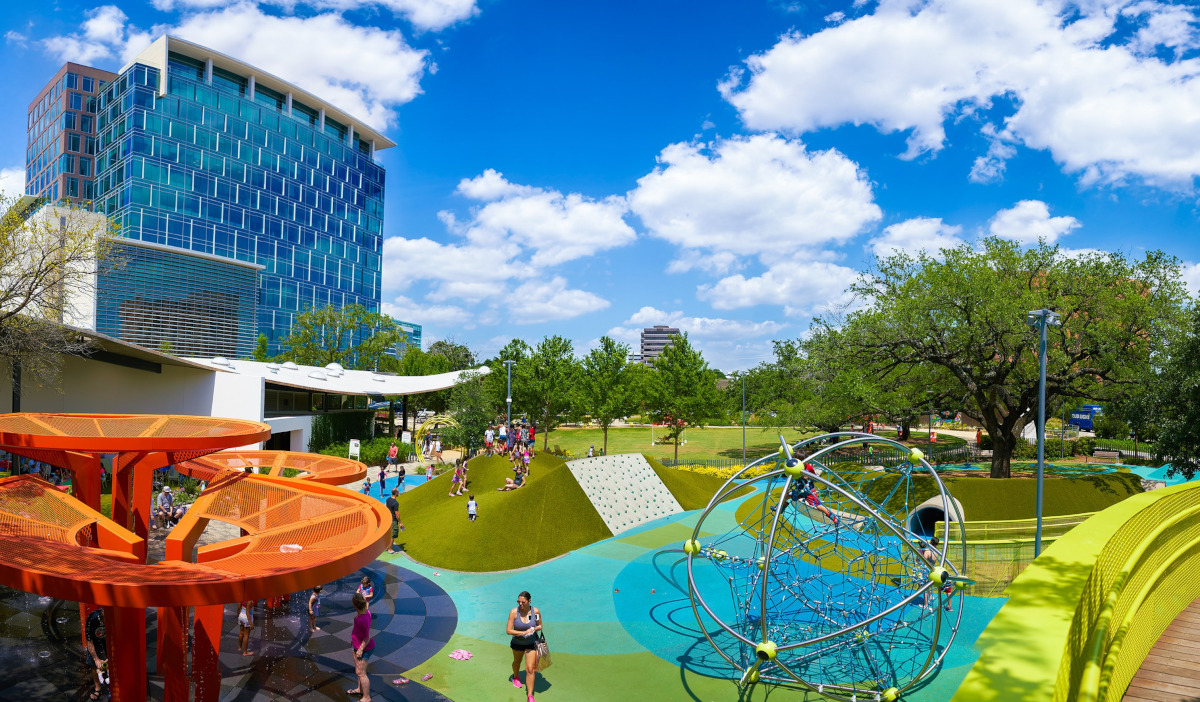 A wide shot of a park on a clear day with playground equipment and high rises in the background