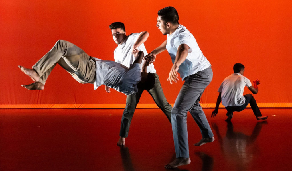 Dancers flip and support each other in front of an orange backdrop