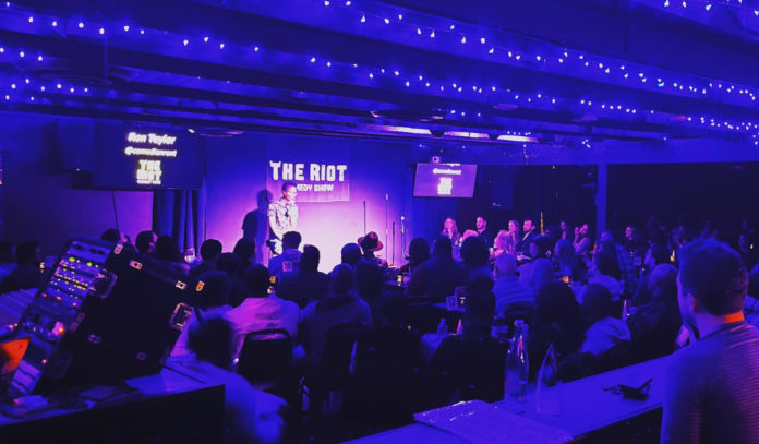 A stage bathed in purple light with a comedian at the mic