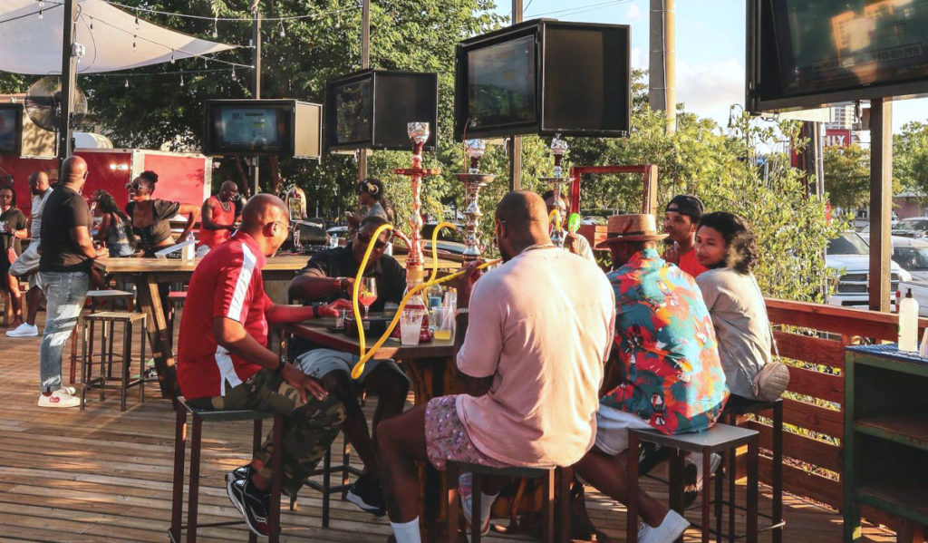 An outdoor patio with hookah setup, TVs and crowds of people