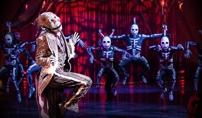 Costumed performers in skeleton suits dance with a main performer at a circus