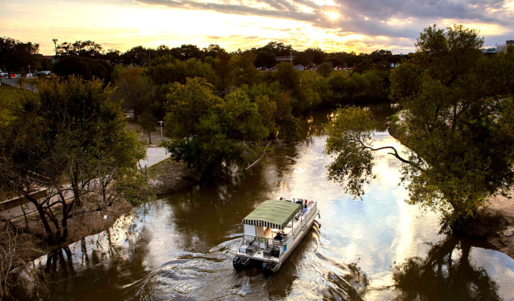 A pontoon boat cruises down Buffalo Bayou at sunset