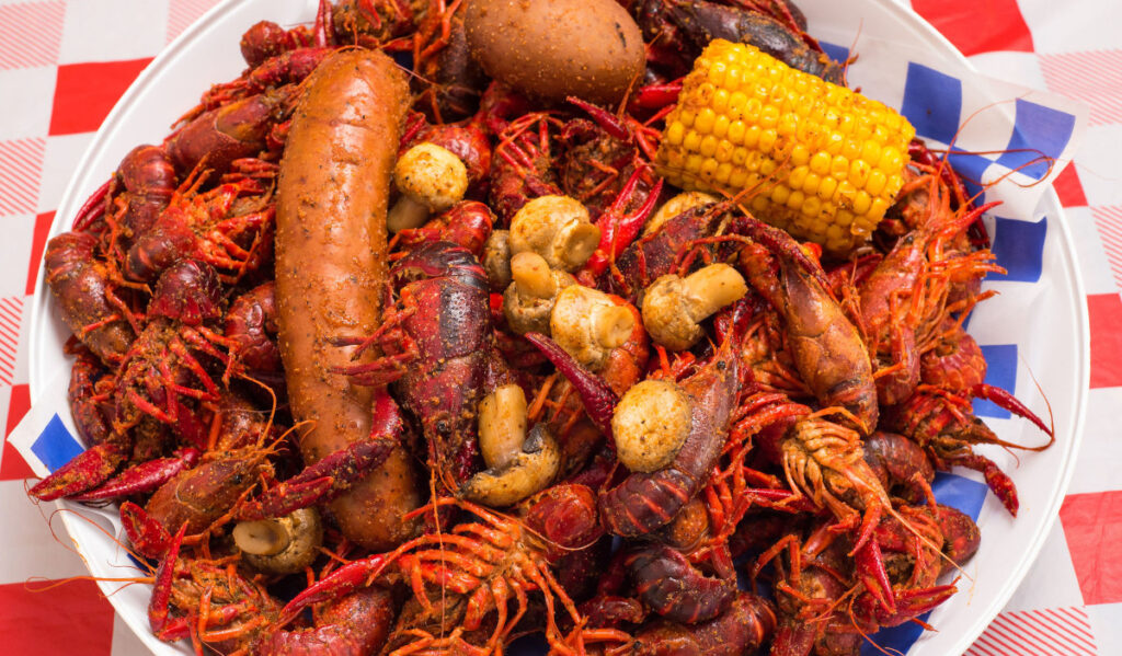 An overhead shot of a plate of crawfish with sausage, corn, mushrooms and potatoes