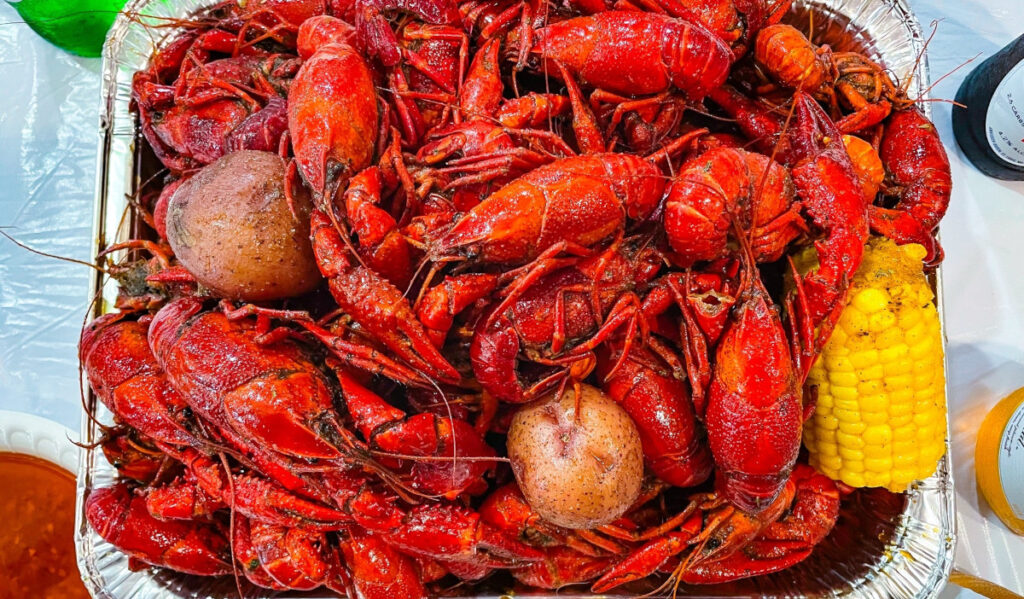 A foil container of fresh crawfish with potatoes and corn