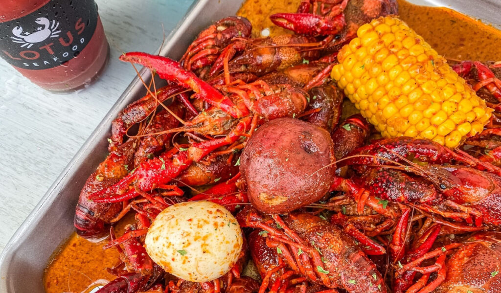 A plate of crawfish with corn, potato and egg and a drink nearby