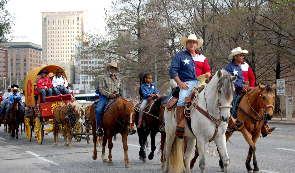 Men and women on horseback ride through Downtown streets, followed by a covered wagon