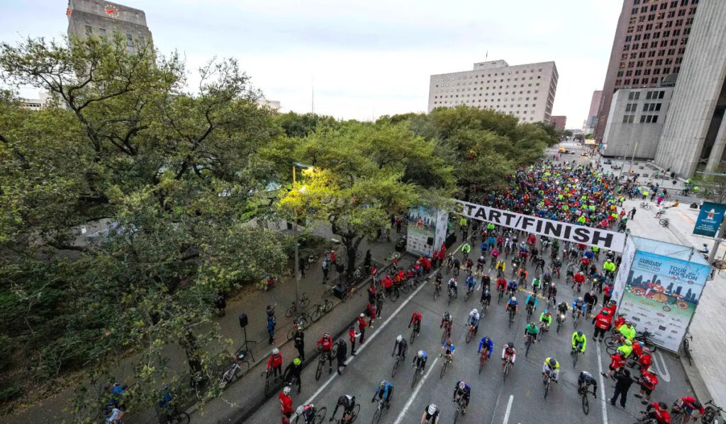 Hundreds of bicyclists roll through a starting line in Downtown Houston