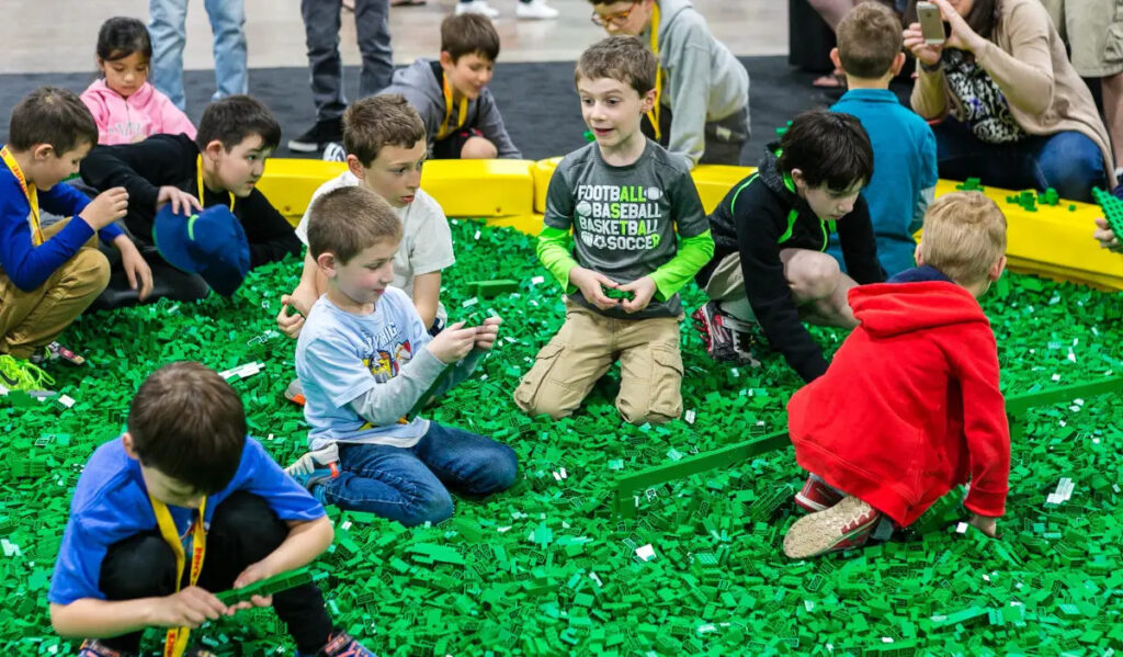 Several kids sit in a pool of green LEGOs