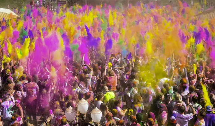 A crowd of festival goers underneath plumes of colored pigment in the air