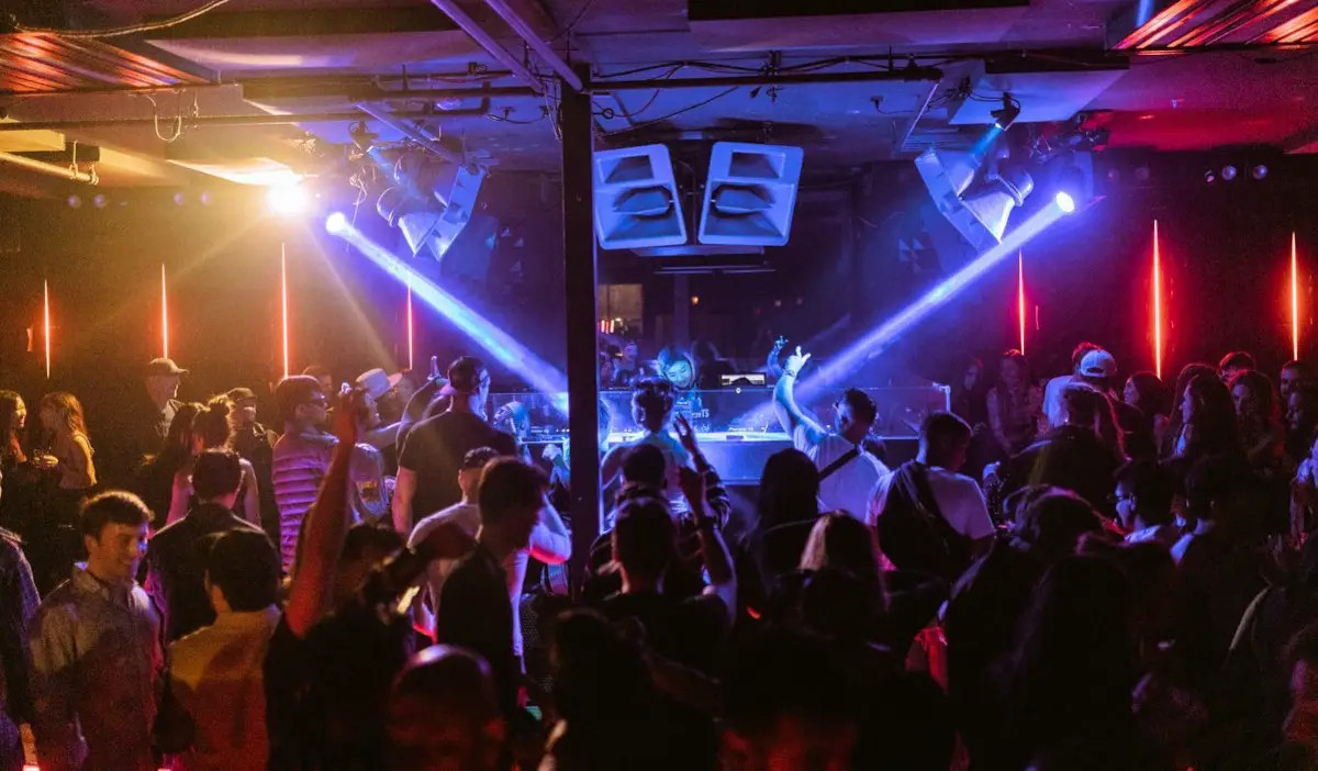 A DJ performs in the middle of a crowded club with beams of light pointed at them