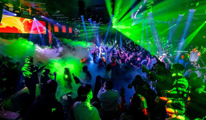 A nightclub interior with green laser lights, smoke machines and crowds of people dancing