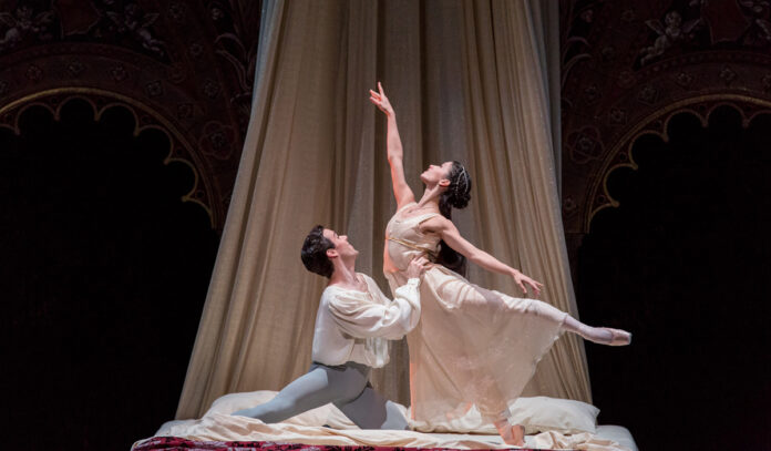 A performer cast as Juliet reaches up as Romeo holds her at the waist