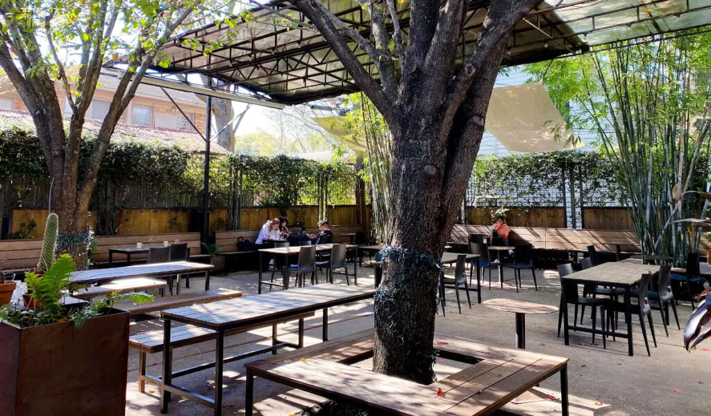 A patio with trees and greenery, and a few patrons at tables