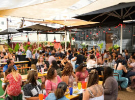 An outdoor patio with patrons eating and a drag performer in the background