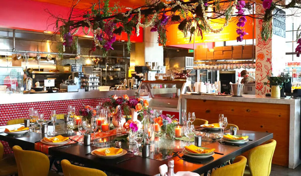 A communal table in a restaurant with garlands of flowers and greenery hanging from above