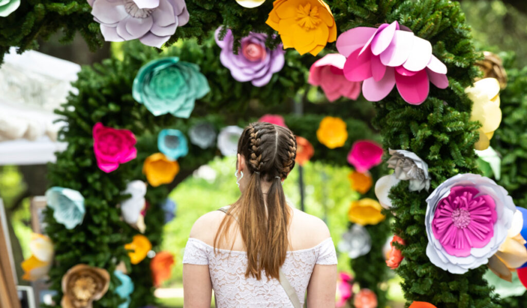 The back of a woman standing in front of colorful flower-craft arches