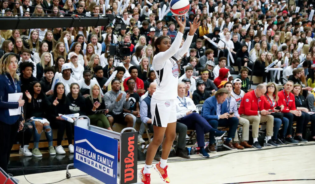 An athlete shoots a three-pointer while the crowd looks on