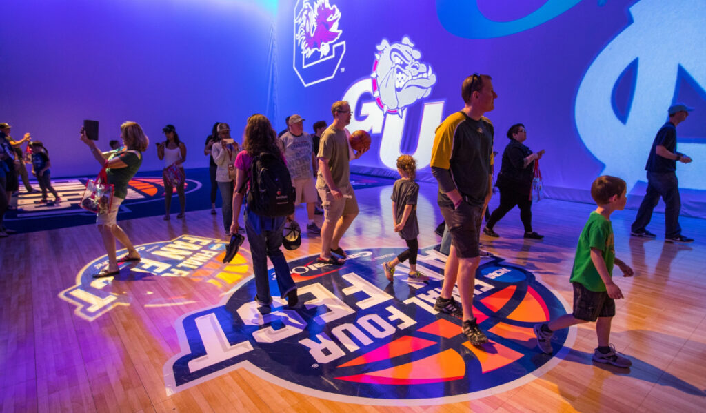 Fans walk through an area with projections of college logos on the walls