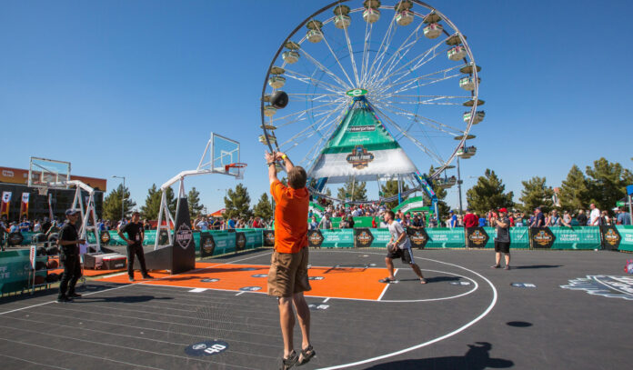 Two people compete in a basketball competition with a Ferris Wheel in the background