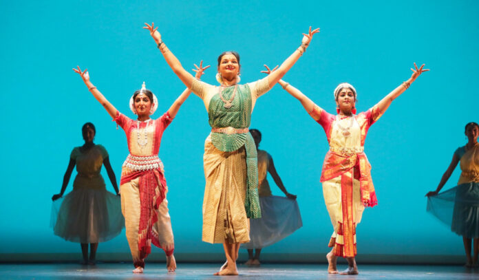 Three Indian performers pose with arms outstretched into the air