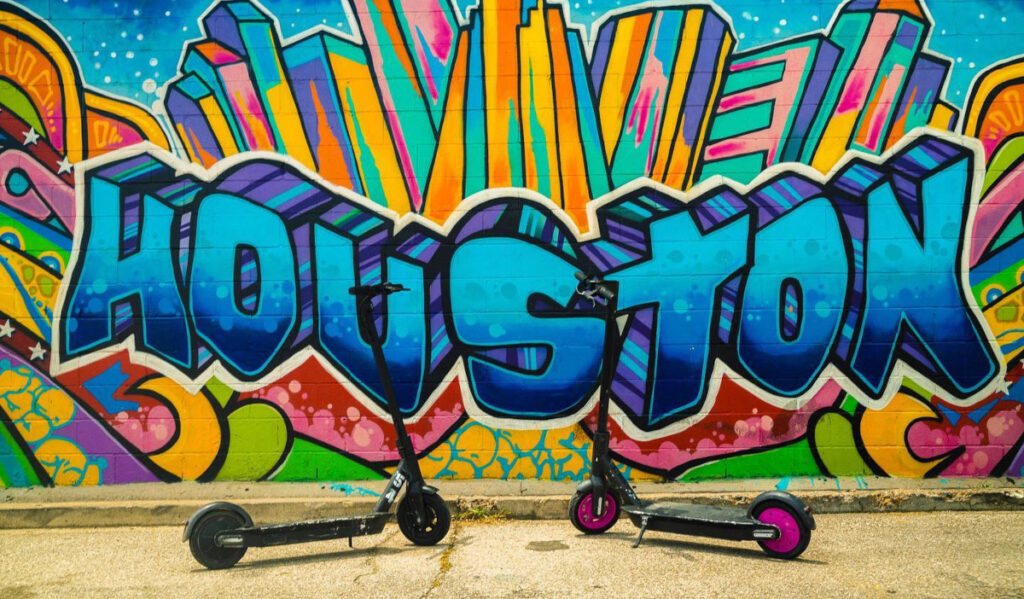 Two scooters standing in front of a "Houston" mural
