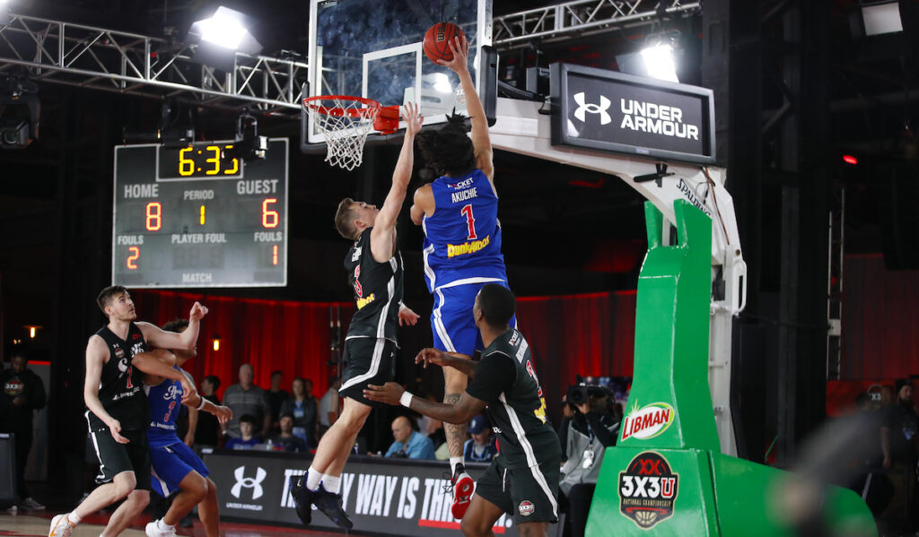 A basketball player rises for a dunk while another tries to block him