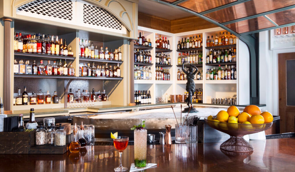 Two drinks sit on a bar with a pile of shaved ice and shelves of liquor behind them