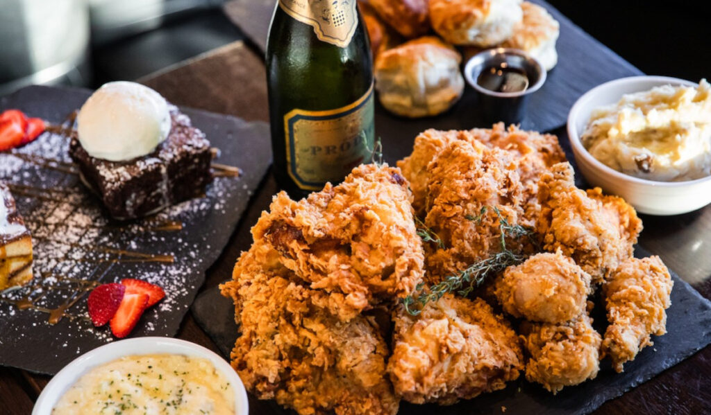 A plate of fried chicken with grits, dessert and a bottle of Champagne