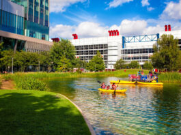 People kayak on water with a skyscraper and convention center in the background
