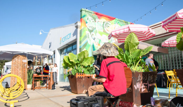 A sidewalk scene with a music performer and visitors browsing vendor booths