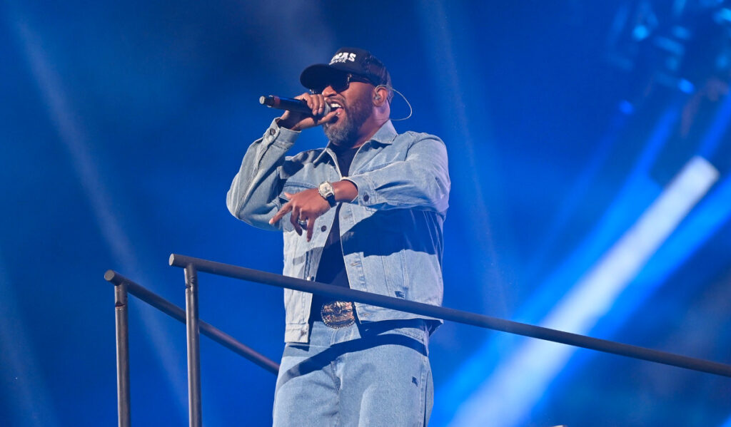 Bun B performs at the Rodeo in a denim jacket with a baseball cap and black glasses