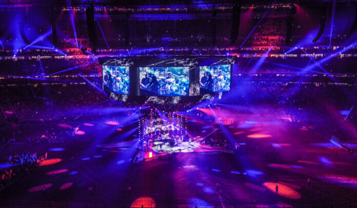 A star-shaped concert stage in a stadium with beams of blue and purple lights around it