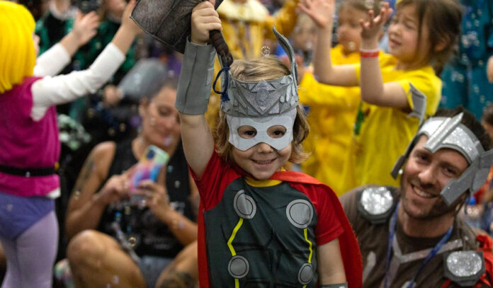 A child dressed as Thor holds a hammer above their head