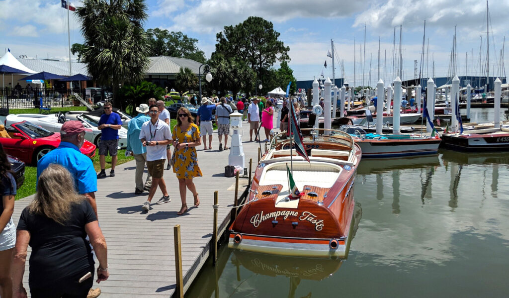 People walk along a pier past display vehicles and boats