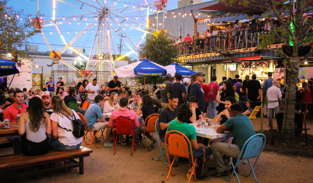 A lively outdoor patio with people conversing and a Ferris Wheel in the background