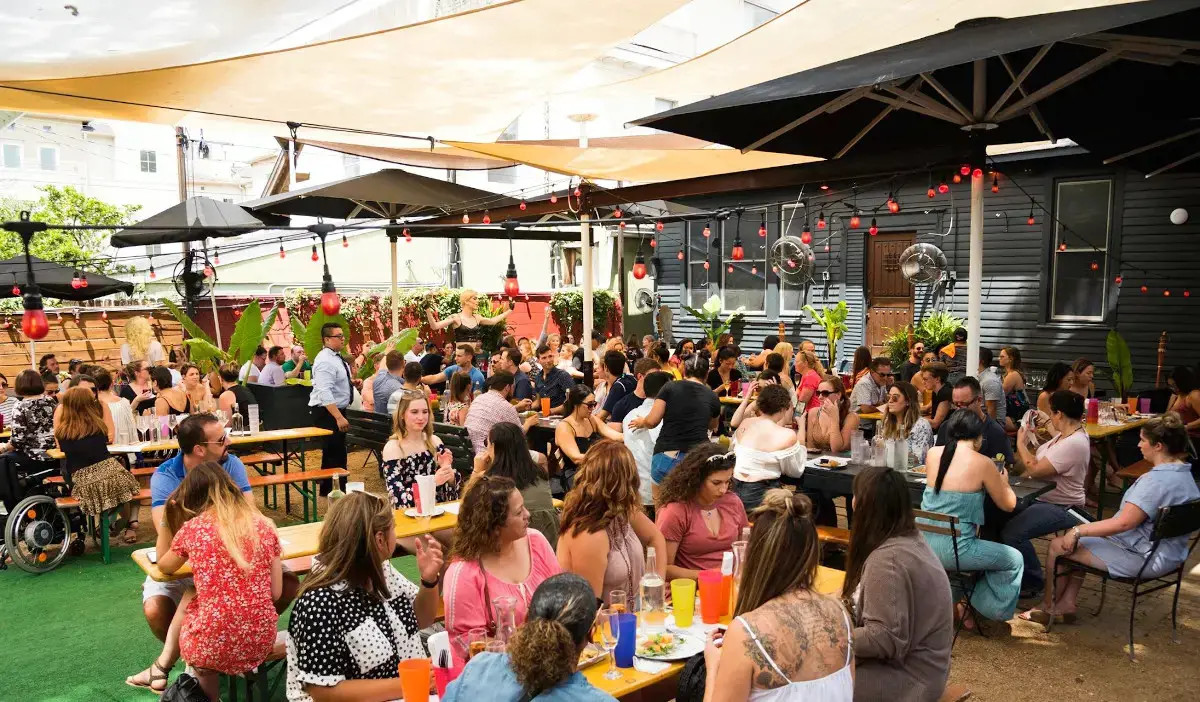 An outdoor patio with patrons eating and a drag performer in the background