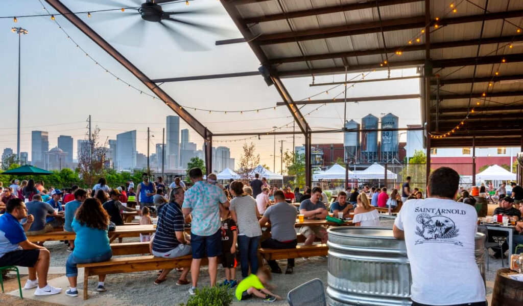A spacious outdoor beer garden with the Downtown Houston skyline in the background