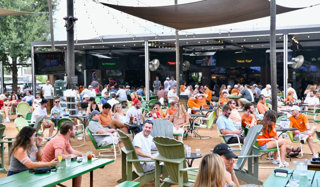 A spacious outdoor patio with fans in University of Texas clothes watching sports