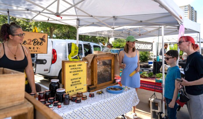 pollinator-festival-urban-harvest-farmers-market-houston-2023-3 Two vendors at a honey booth talk with customers