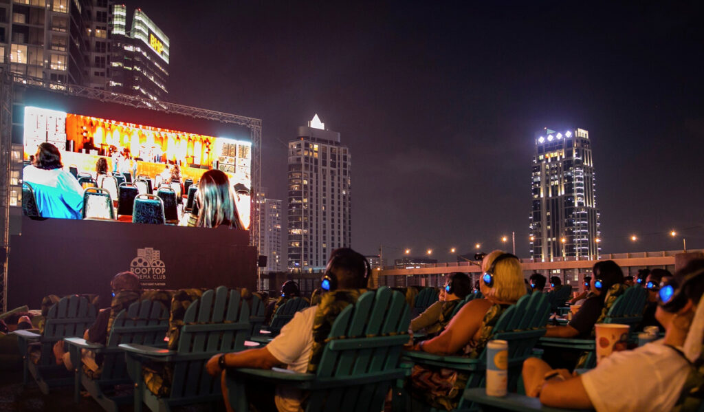 A rooftop movie screening at night with skyscrapers behind 