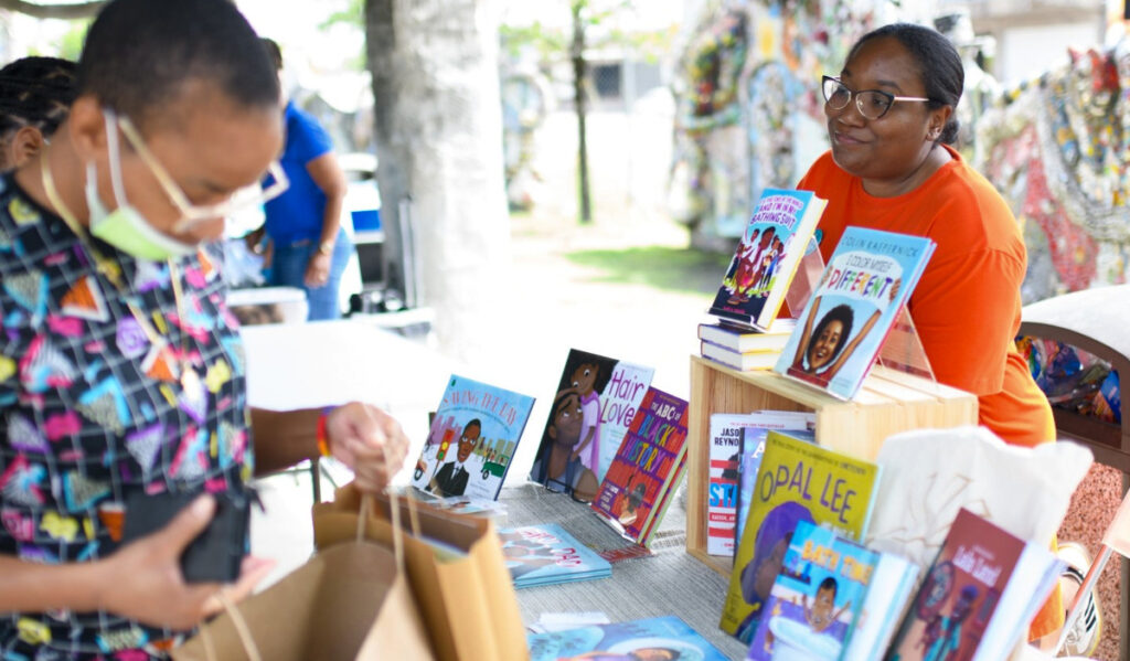 A book vendor looks on as a visitor leaves with a bag of books