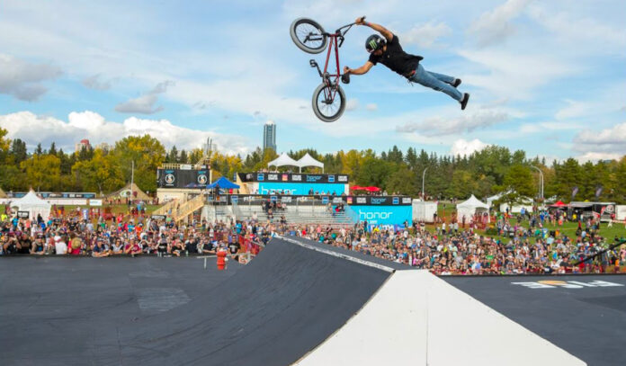 A BMX rider performs a mid-air trick while a crowd watches on